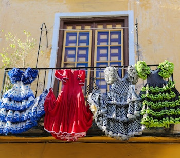 Farverige traditionelle flamenco-kjoler hængende udenfor et historisk hus i Malaga, der viser den autentiske andalusiske kultur
