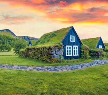 Idylliske tørvehuse med græstag i Skogar landsby under en dramatisk solopgang i Sydisland, perfekt til en eventyrlig rejseoplevelse
