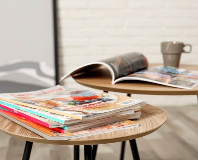 Elegante træborde med farverige rejsemagasiner og en kaffekop der skaber et hyggeligt læsehjørne i lounge-området