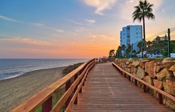 En træsti på stranden i solnedgangstid ved Mijas Costa, Andalusien, med udsigt over havet og den farverige himmel.