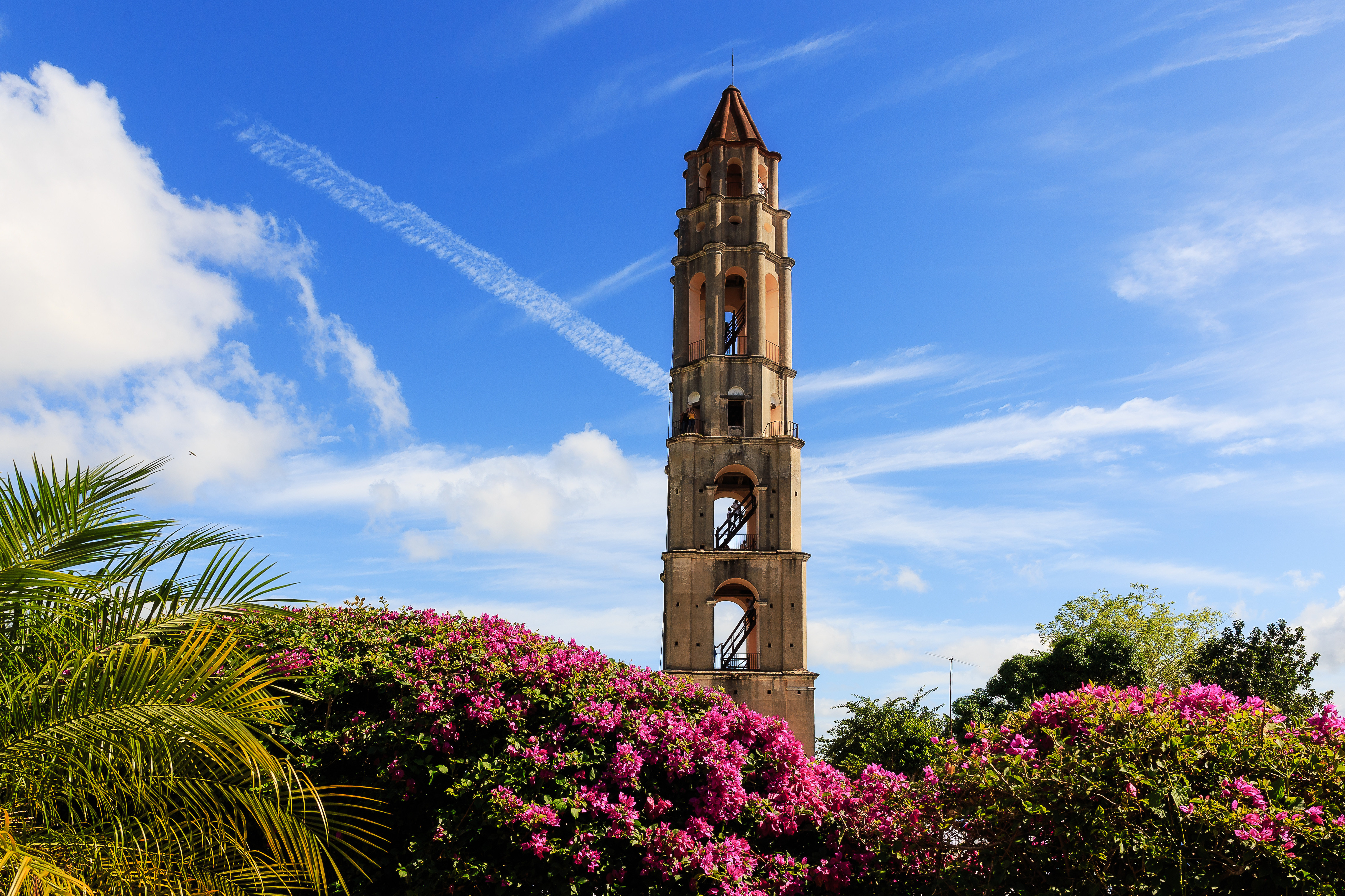 Historisk klokketårn i Trinidad Cuba med tropiske blomster og palmer under blå himmel
