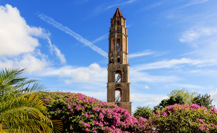 Historisk klokketårn i Trinidad Cuba med tropiske blomster og palmer under blå himmel