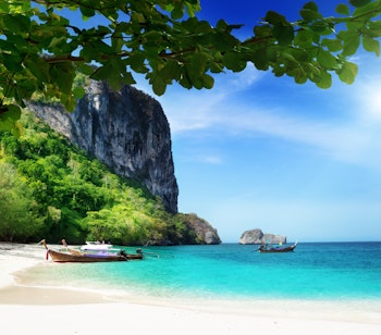 Idyllisk hvid sandstrand med traditionelle longtail-både ved det turkisblå vand på Poda-øen i Thailand, omgivet af majestætiske kalkstensklipper