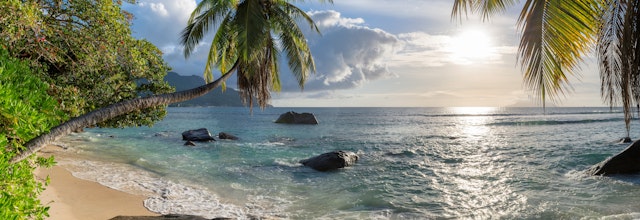 Idyllisk panoramaudsigt over Beau Vallon stranden på Mahe i Seychellerne med palmetræer, krystalklart vand og karakteristiske granitsten ved solnedgang