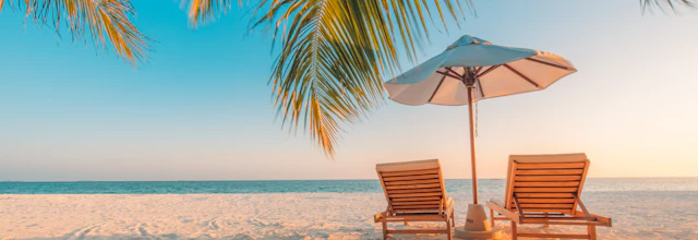 Tropisk paradis strand med palmer, liggestole og parasol ved solnedgang