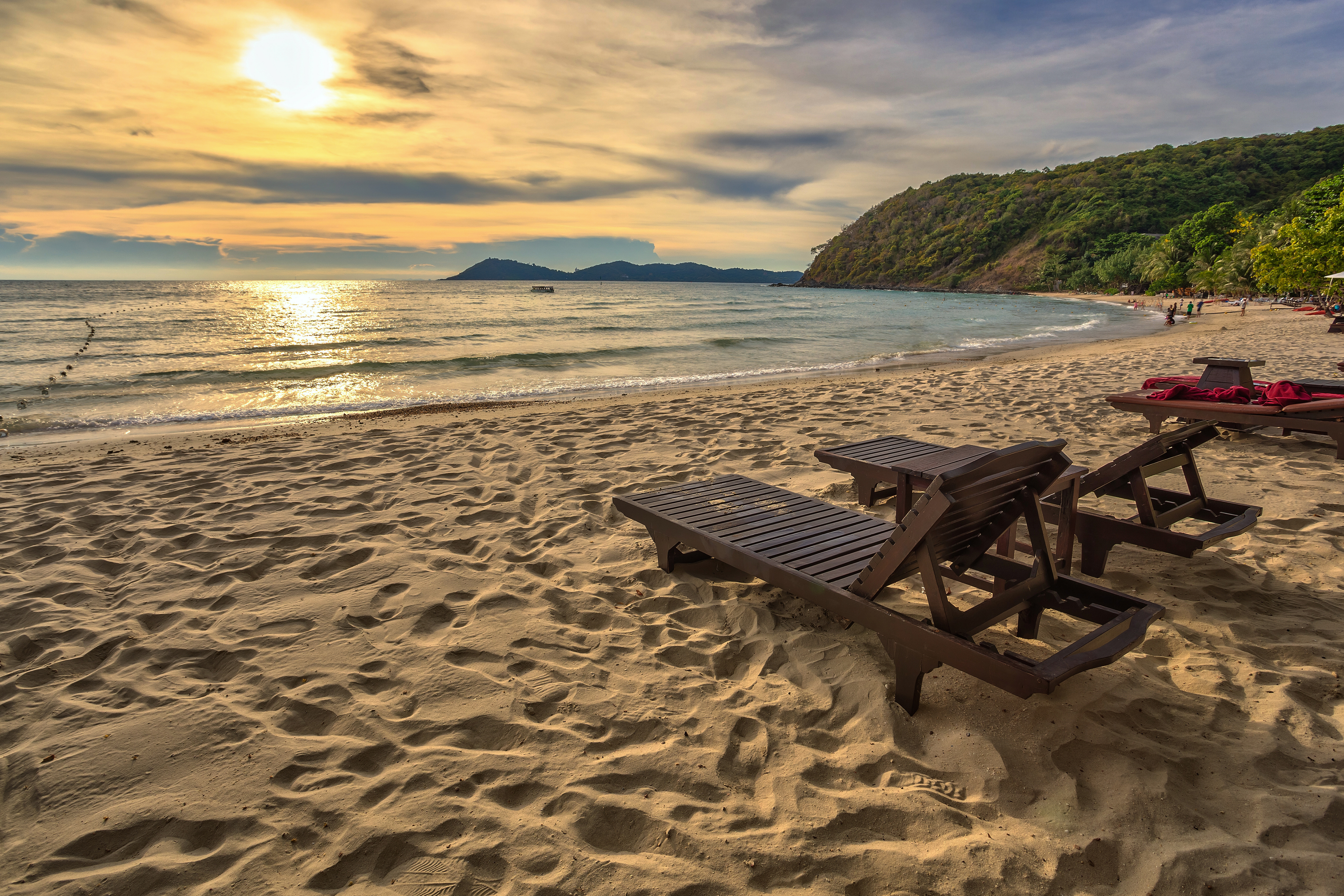 Tropisk strand med solnedgang og træliggestole på gyldent sand i Thailand