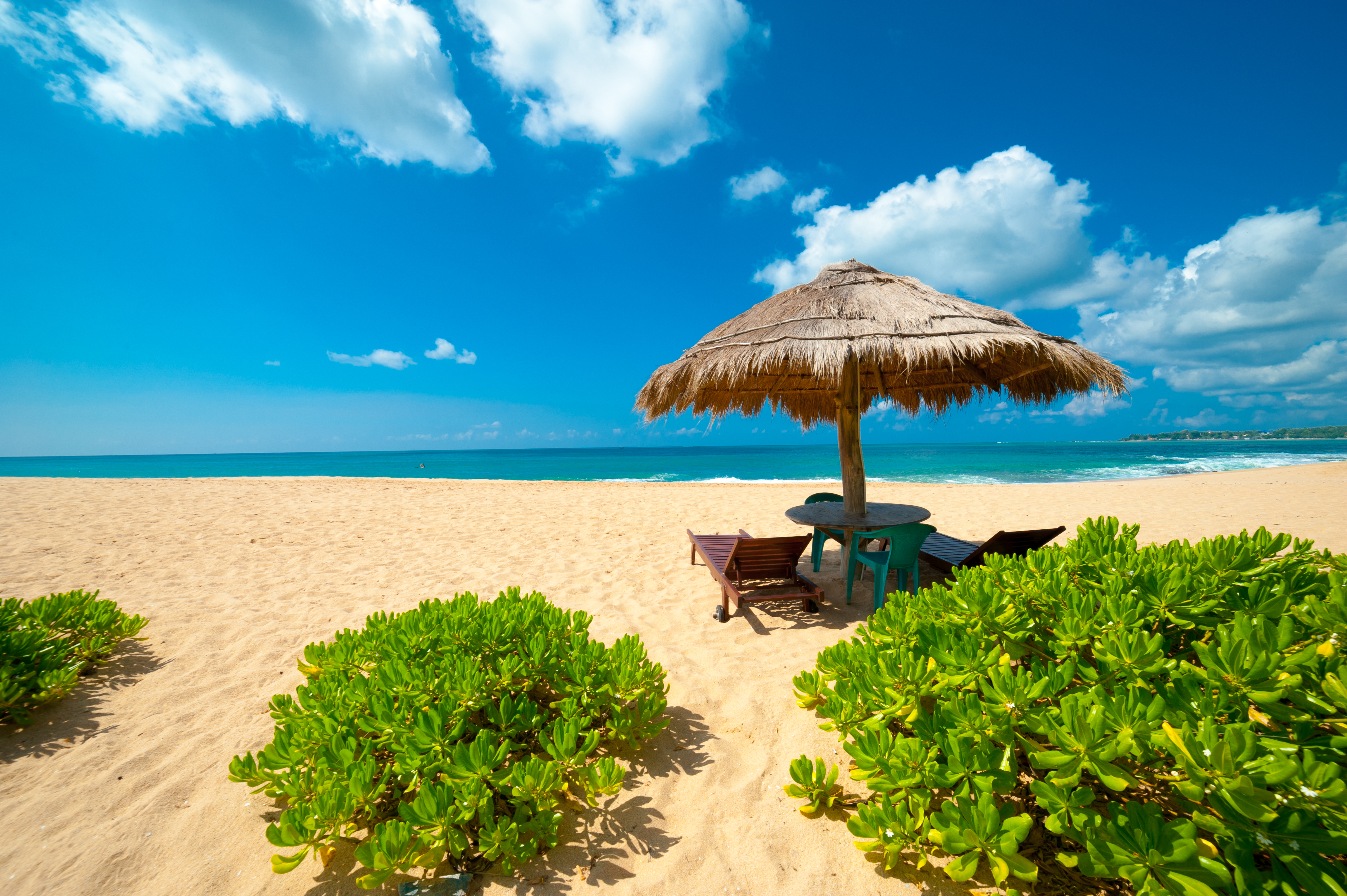 Idyllisk tropisk strand i Sri Lanka med stråtækt parasol, solsenge, gyldent sand og turkisblåt hav under klar himmel
