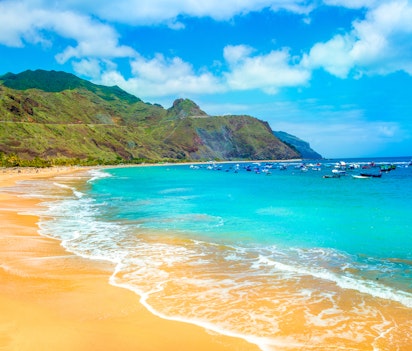 Idyllisk tropisk strand med turkisblåt vand, gyldent sand og frodige grønne bjerge - perfekt til en afslappende ferie i paradis