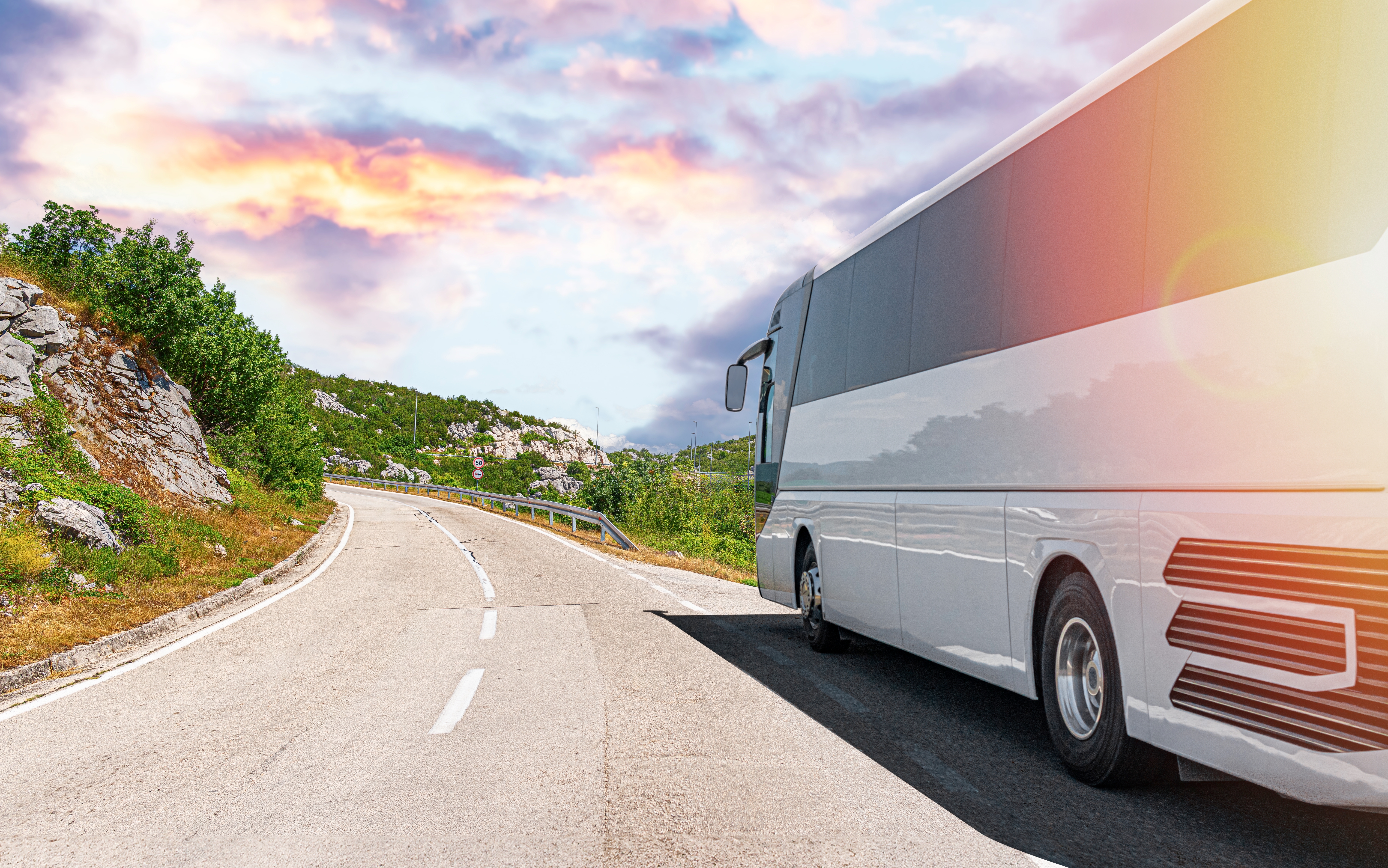 Turistbus kører på smuk bjergvej ved solnedgang under ferietur i Europa