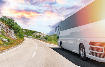Turistbus kører på smuk bjergvej ved solnedgang under ferietur i Europa