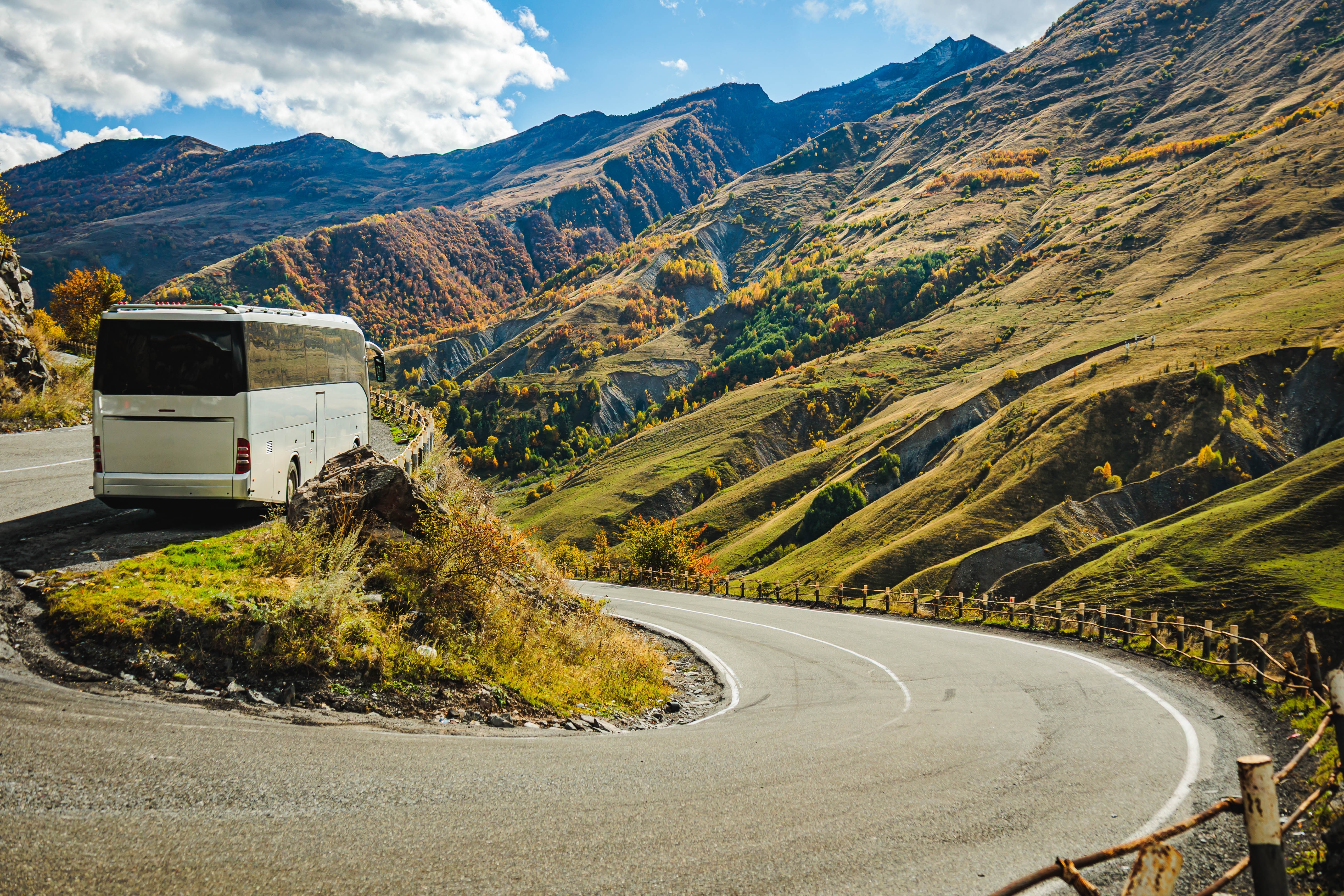 Hvid turistbus kører ad en bugtet bjergvej gennem det farverige efterårslandskab i Kaukasus-regionen i Georgien