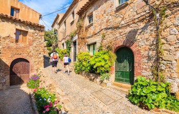Par af turister med rygsække udforsker de smalle, charmerende gader i den historiske gamle bydel i Tossa de Mar, Costa Brava