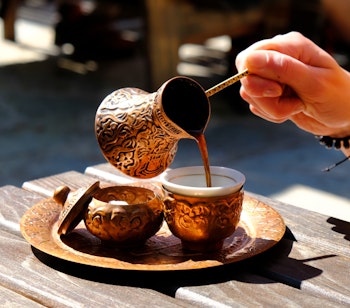 Traditionel tyrkisk kaffe hældes fra ornamenteret kobberkande i dekorativ kop på træbord