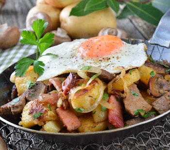 Traditionel tyrolsk Groestl med stegte kartofler, kød, bacon, svampe og spejlæg - autentisk østrigsk bjergmad serveret i en rustik pande