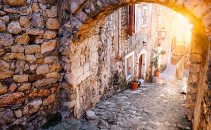 Idyllisk stenbue og blomsterkrukker langs brostensbelagt gade i den historiske bydel af Ulcinj ved solnedgang