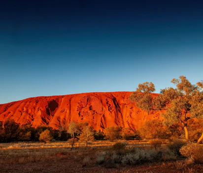 Uluru Ayers Rock lyser roedt ved solnedgang i australsk oekenlandskab