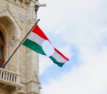 Ungarsk flag med hul foran parlamentsbygningen i Budapest, symboliserer revolutionen i 1956 og kampen for frihed