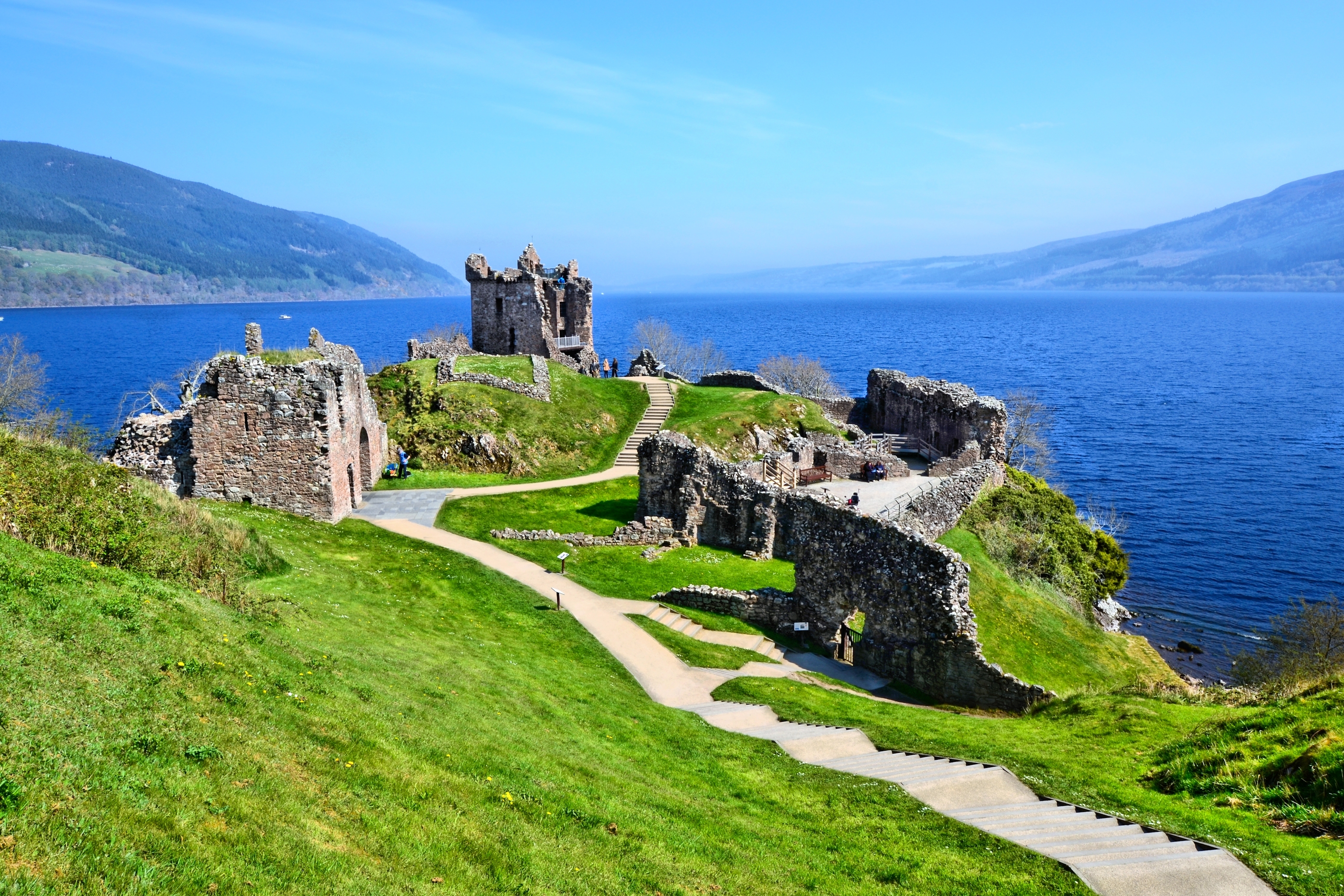 Historiske Urquhart Castle ruiner ved Loch Ness i de skotske højlande med grønne marker og blå sø
