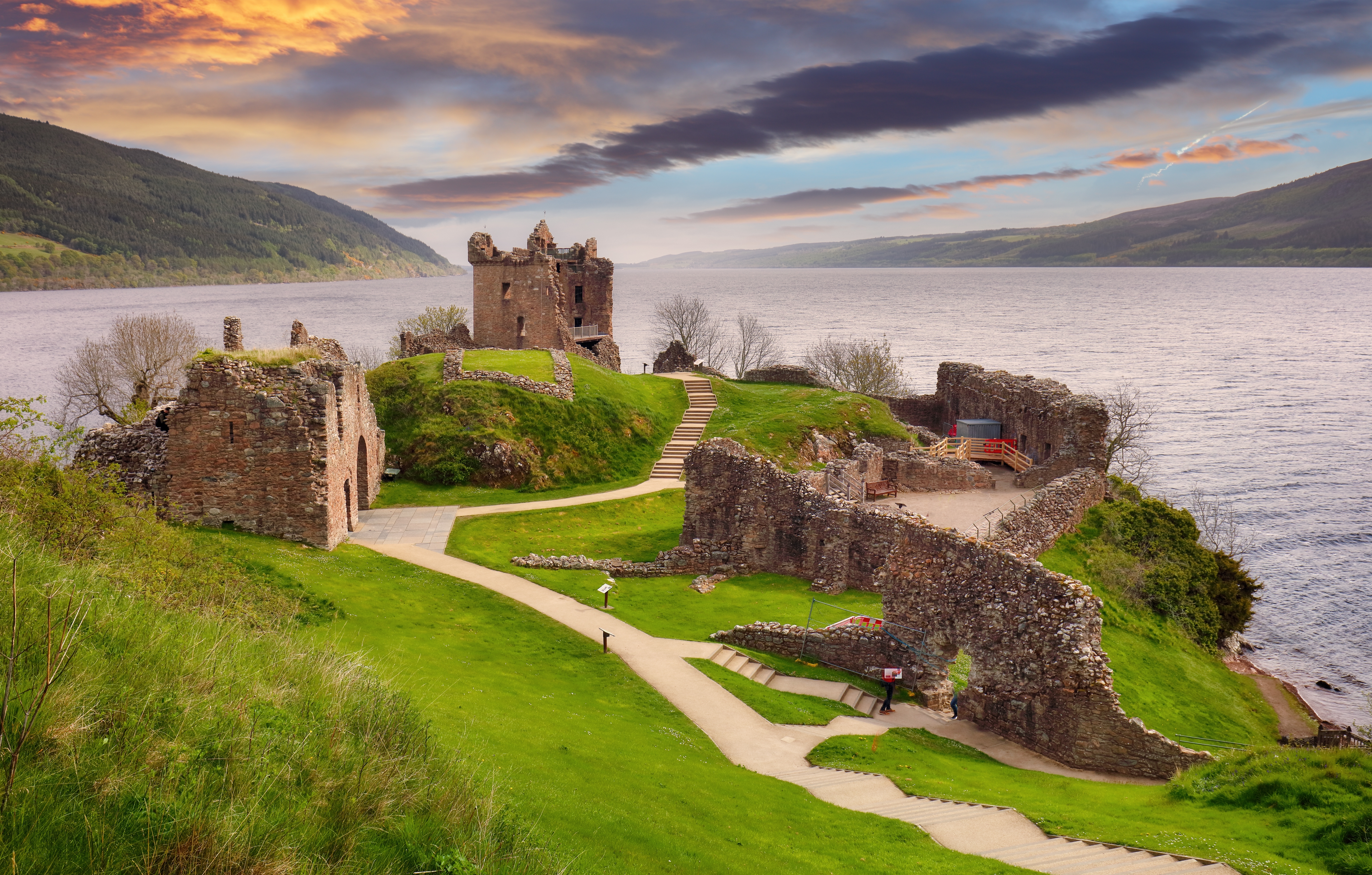 Urquhart Slots historiske ruiner ved solnedgang over Loch Ness i det skotske højland med dramatisk orange himmel
