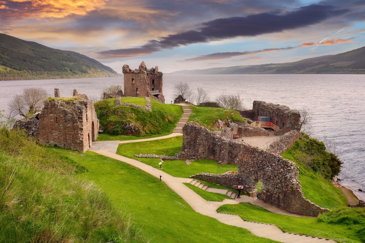Urquhart Slots historiske ruiner ved solnedgang over Loch Ness i det skotske højland med dramatisk orange himmel