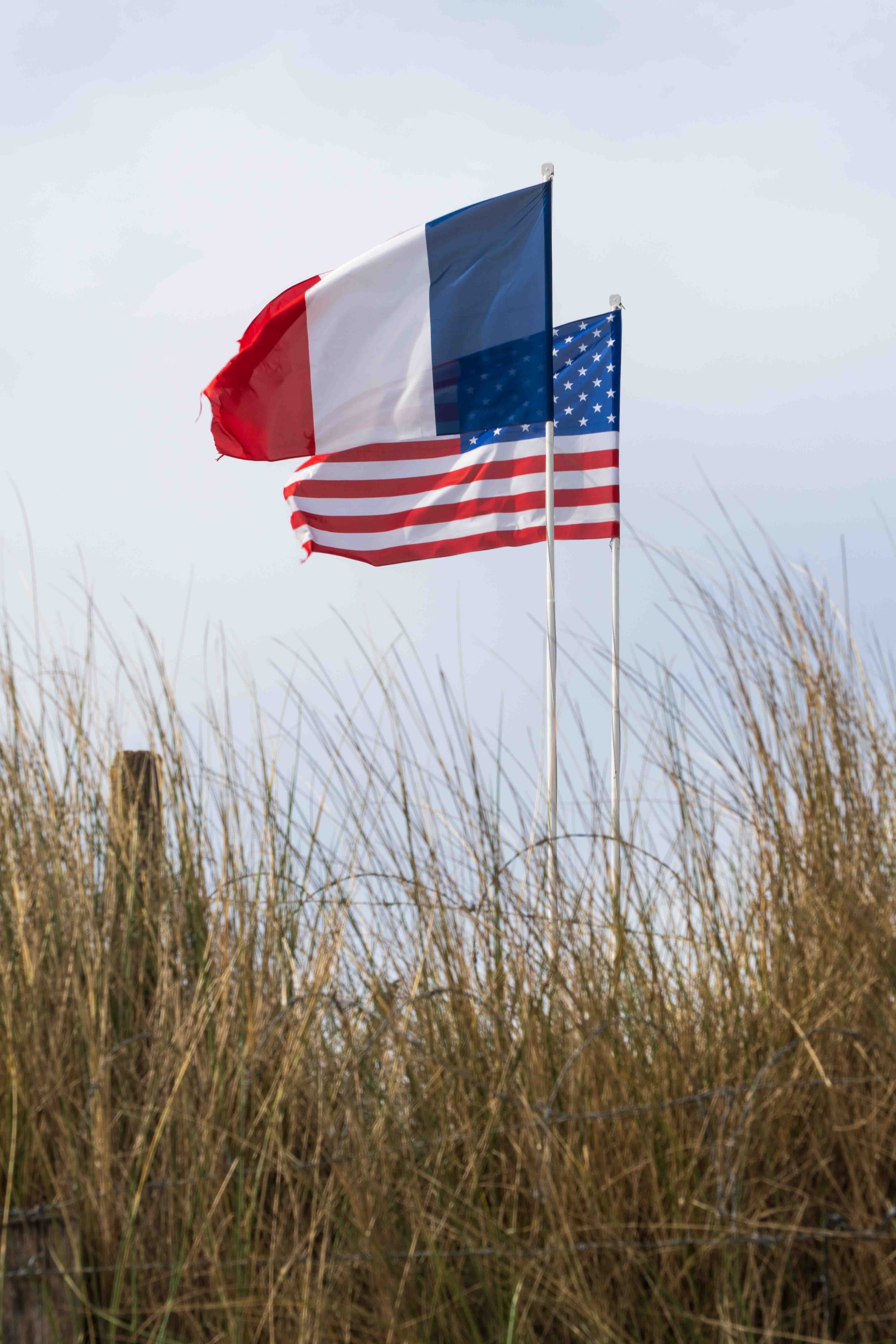 Fransk og amerikansk flag vajer side om side på Utah Beach i Normandiet, Frankrig, til minde om D-dag landgangen med kystnære klitgræsser i forgrunden