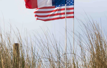 Fransk og amerikansk flag vajer side om side på Utah Beach i Normandiet, Frankrig, til minde om D-dag landgangen med kystnære klitgræsser i forgrunden