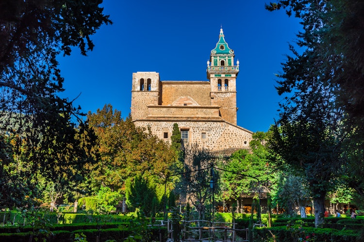 Det historiske Valldemossa-kloster med grønt spir og stentårn omgivet af frodige haver på Mallorca i Spanien