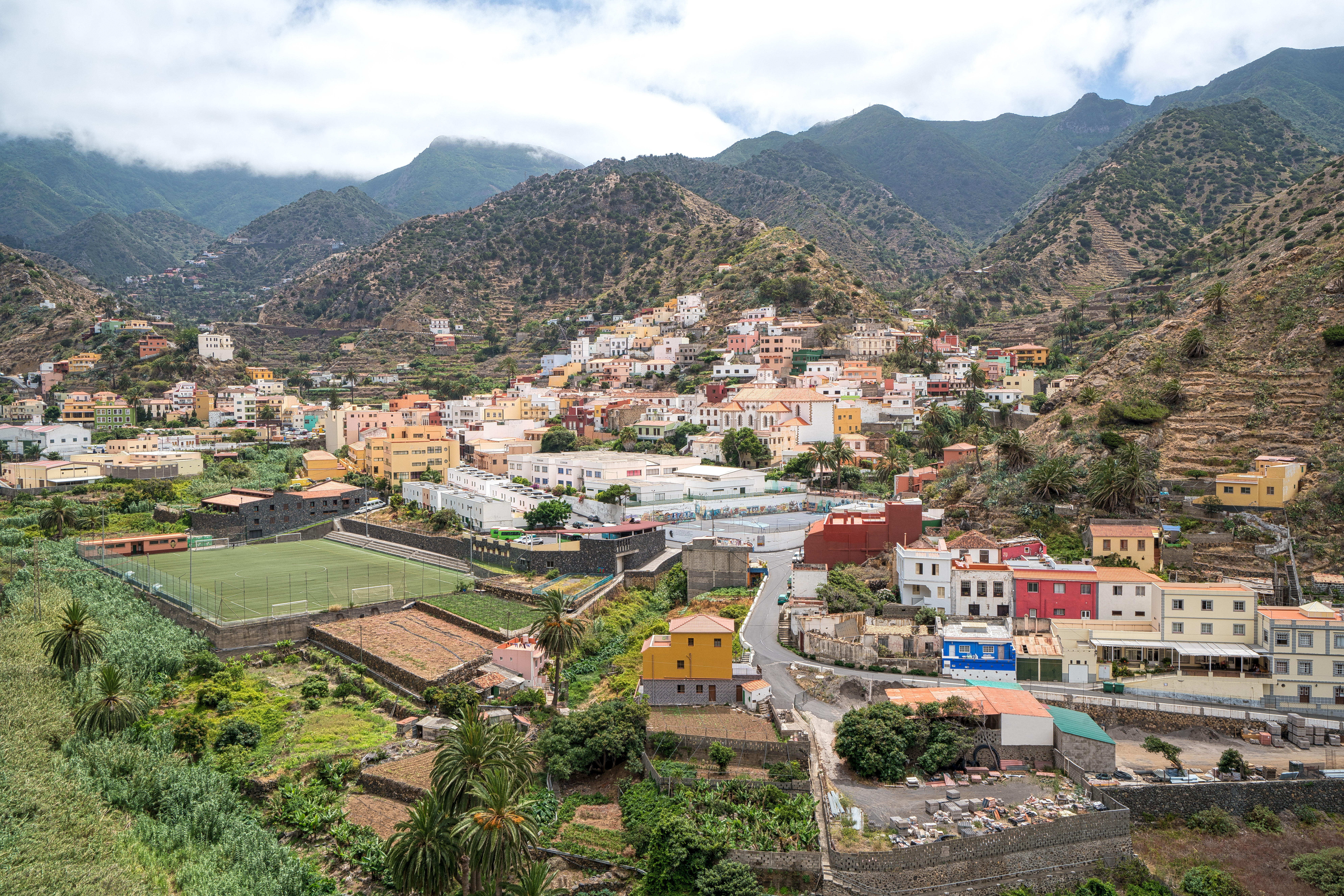 Panoramaudsigt over Vallehermoso-dalen med hvide bygninger omgivet af grønne terrasser og de skyindhyllede Cumbre de Chijere-bjerge på La Gomera
