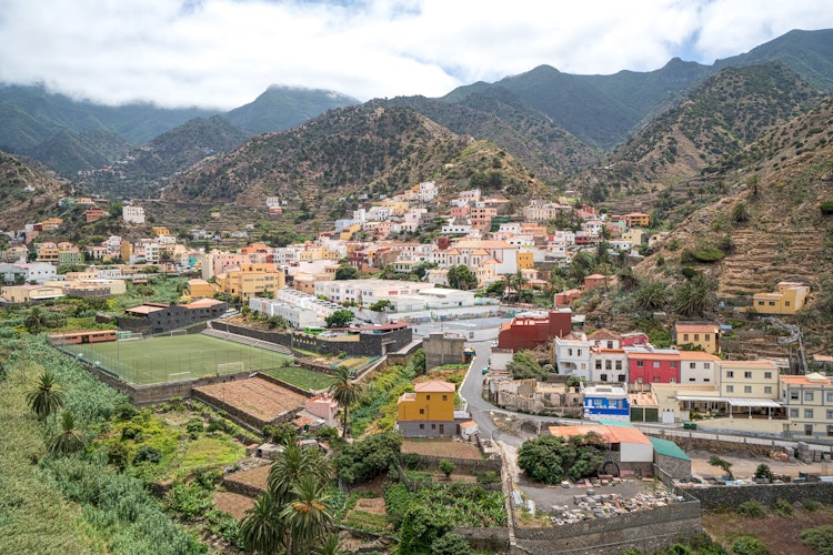 Panoramaudsigt over Vallehermoso-dalen med hvide bygninger omgivet af grønne terrasser og de skyindhyllede Cumbre de Chijere-bjerge på La Gomera