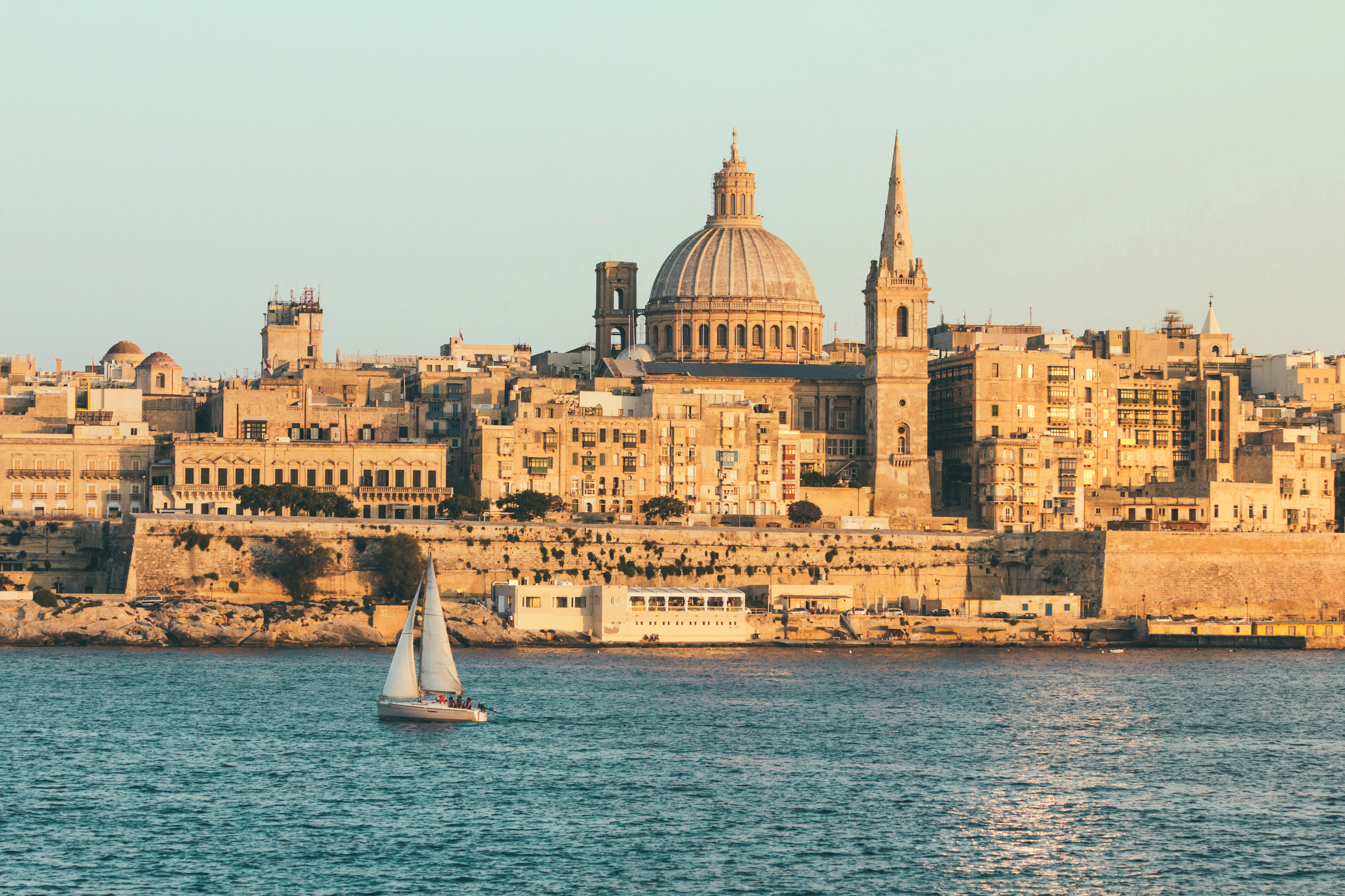 Valletta Maltas smukke kystlinje med St. Pauls Katedral og en sejlbåd på Middelhavet i gyldent aftenlys