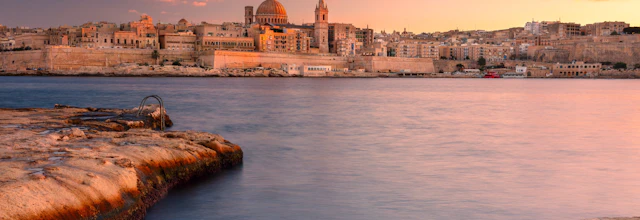 Betagende solnedgangsudsigt over Valletta, Maltas historiske hovedstad, med UNESCO-beskyttet barokarkitektur, gyldne bygninger og havnefront badet i det varme efterårsaftenlys