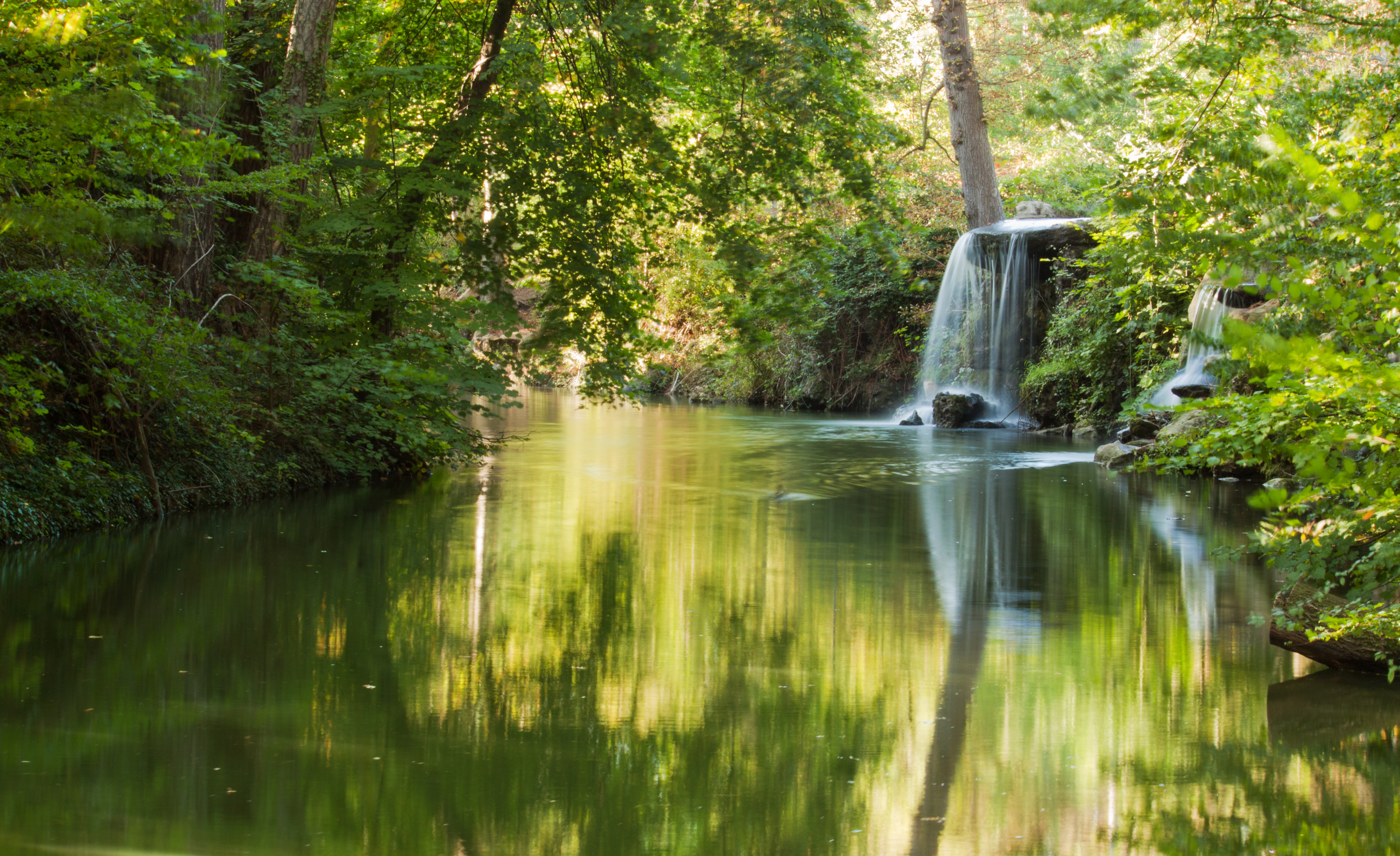 Idyllisk vandfald i Bois de Vincennes parken i Paris med smukke refleksioner i vandet og grøn vegetation