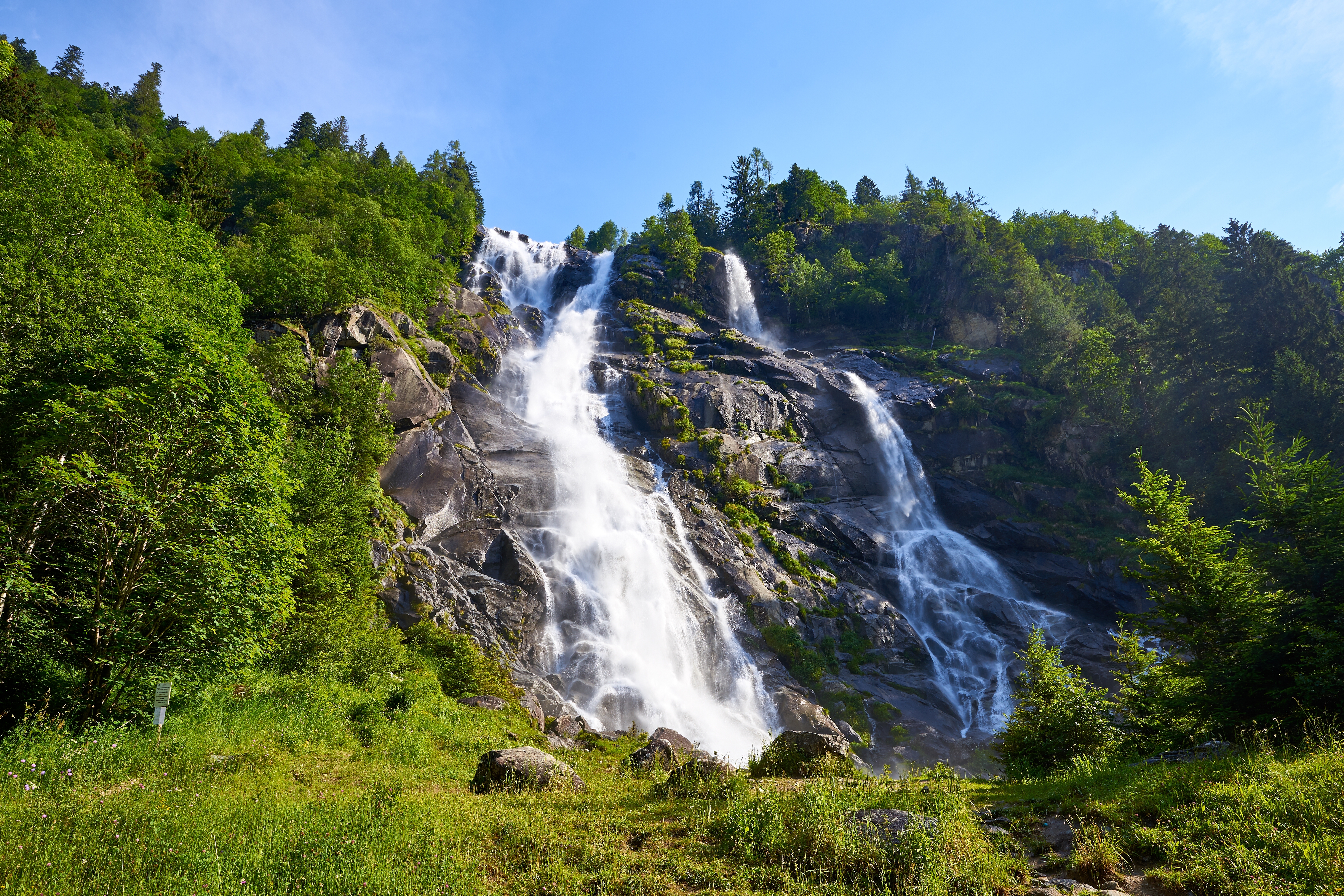 Smukt vandfald i Val Genova, Trentino i de italienske alper, omgivet af frodig grøn skov og klare blå himmel