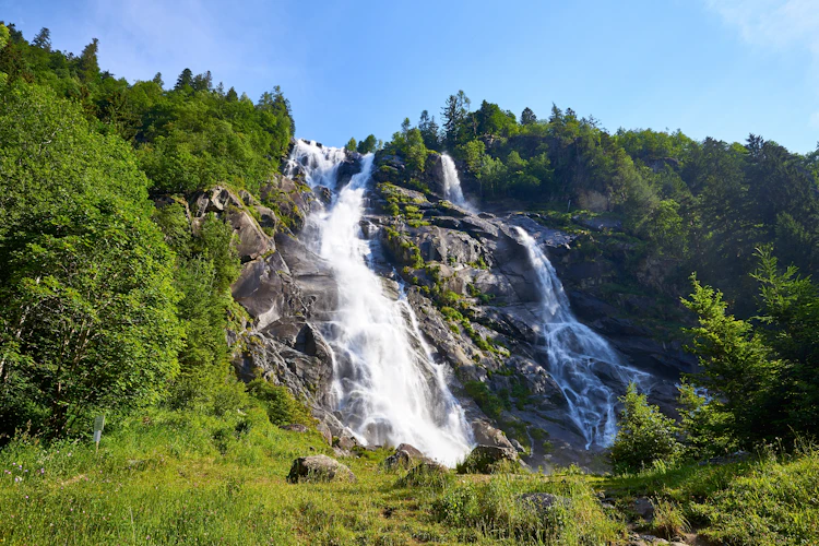 Smukt vandfald i Val Genova, Trentino i de italienske alper, omgivet af frodig grøn skov og klare blå himmel