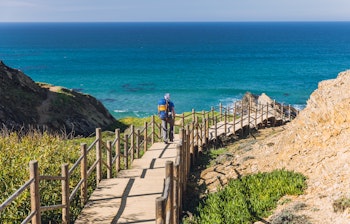 Mand vandrer på den maleriske kyststi Rota Vicentina i Sydportugal med udsigt over Atlanterhavet og dramatiske klipper