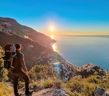 Vandrer med rygsæk nyder solopgangen fra Gudernes Sti mellem Positano og Praiano på Amalfikysten i Italien