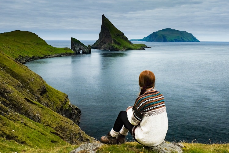 Kvindelig vandrer nyder en pause med udsigt over de dramatiske klippeformationer på Vagar Ø, Færøerne