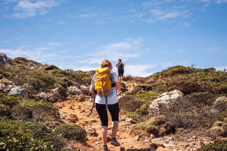 To kvindelige vandrere med rygsæk udforsker de dramatiske kystklinter i Algarve, Portugal på aktiv sommerferie