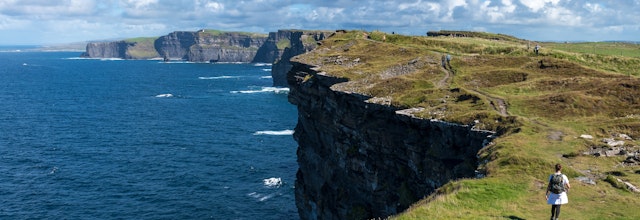 Kvinde vandrer langs den imponerende kyststi ved Cliffs of Moher i Galway, Irland med udsigt over Atlanterhavet