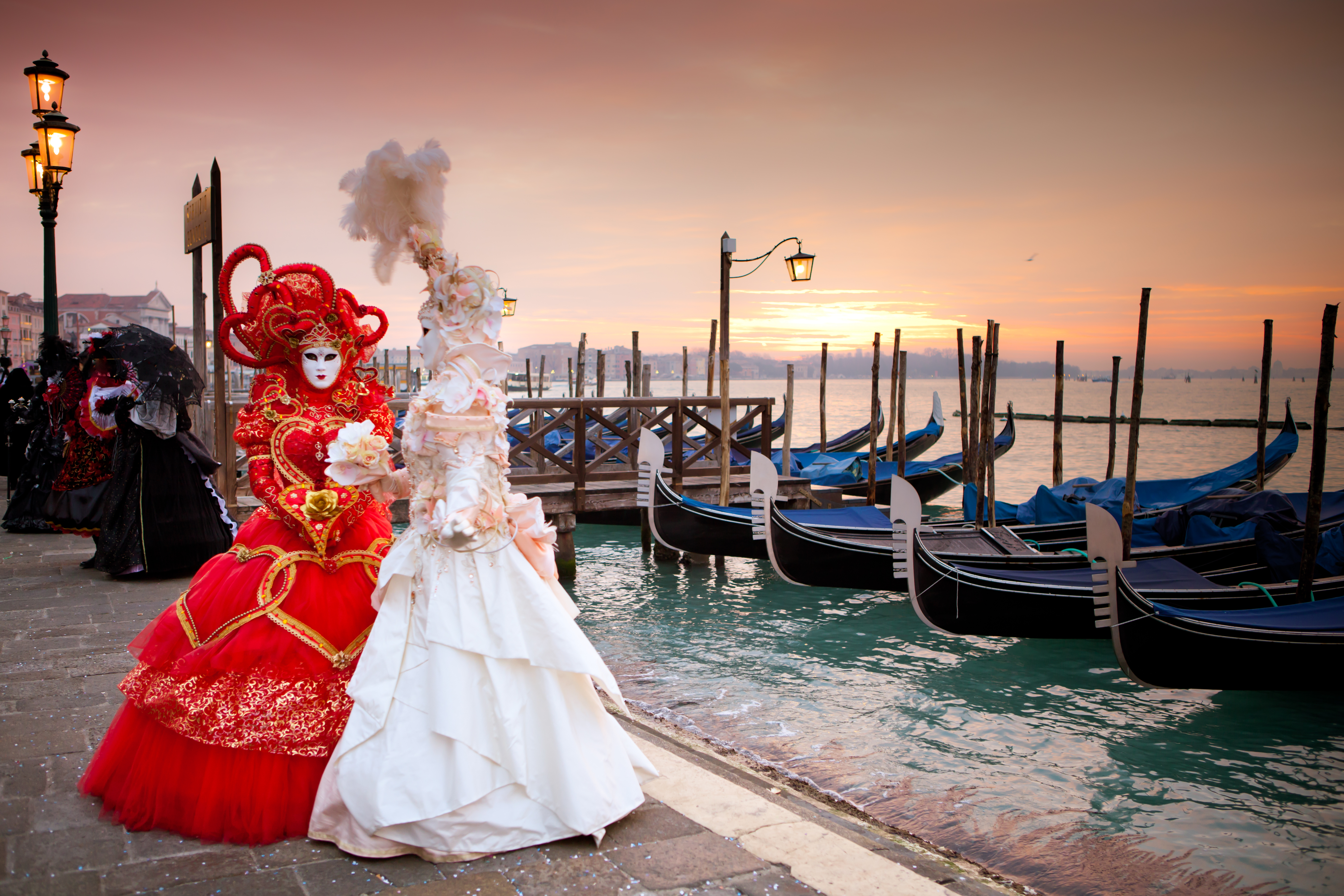 Elegante karnevalskostumer med masker ved gondoler i Venedig ved solnedgang
