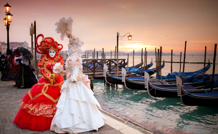 Elegante karnevalskostumer med masker ved gondoler i Venedig ved solnedgang
