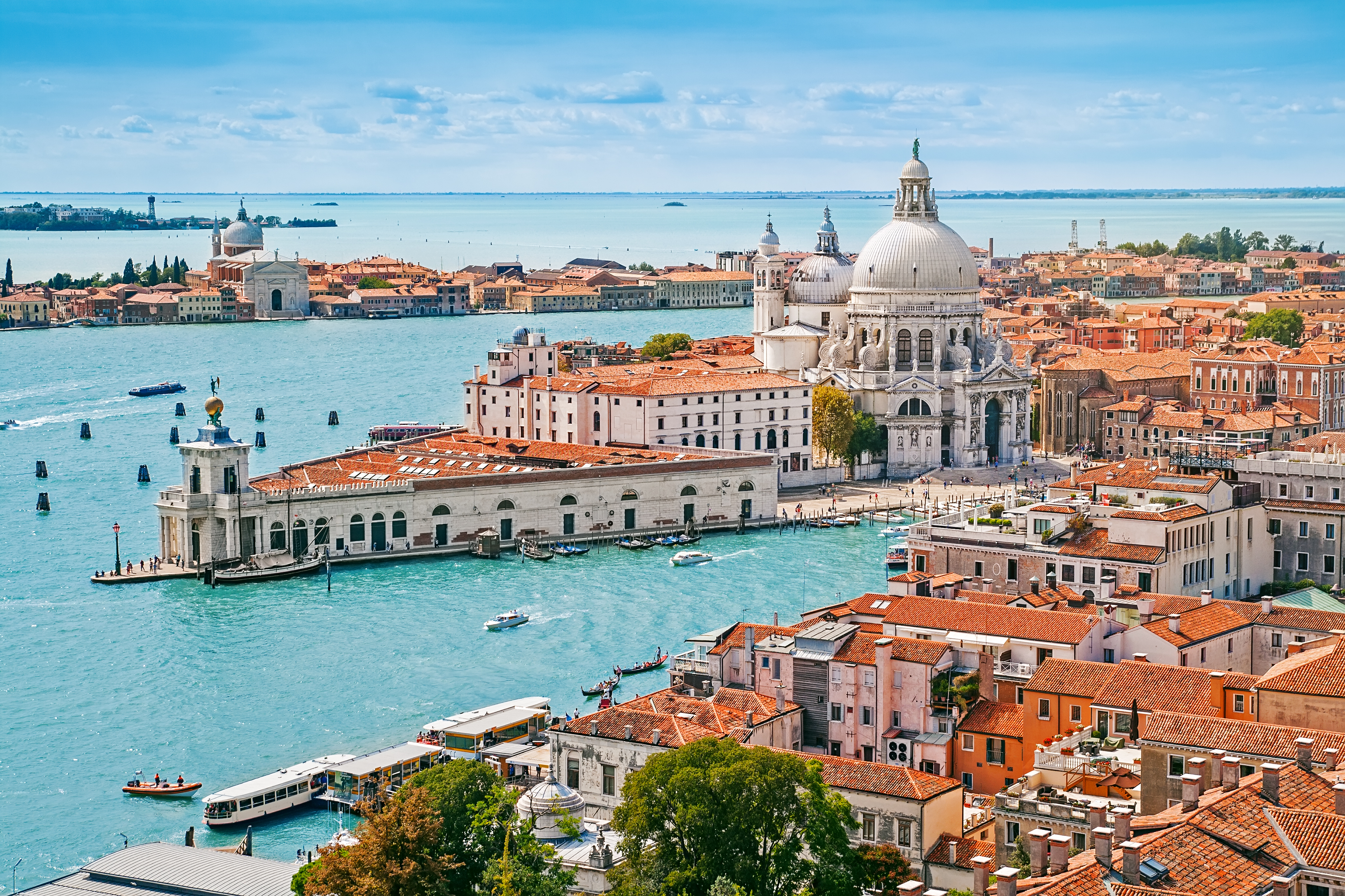Betagende panoramisk luftfoto over Venedigs bylandskab med den ikoniske kuppel på Santa Maria della Salute kirken, der spejler sig i de turkise kanaler