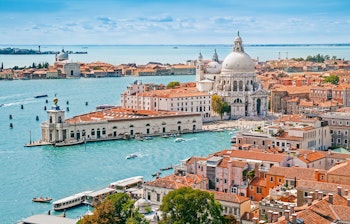 Betagende panoramisk luftfoto over Venedigs bylandskab med den ikoniske kuppel på Santa Maria della Salute kirken, der spejler sig i de turkise kanaler