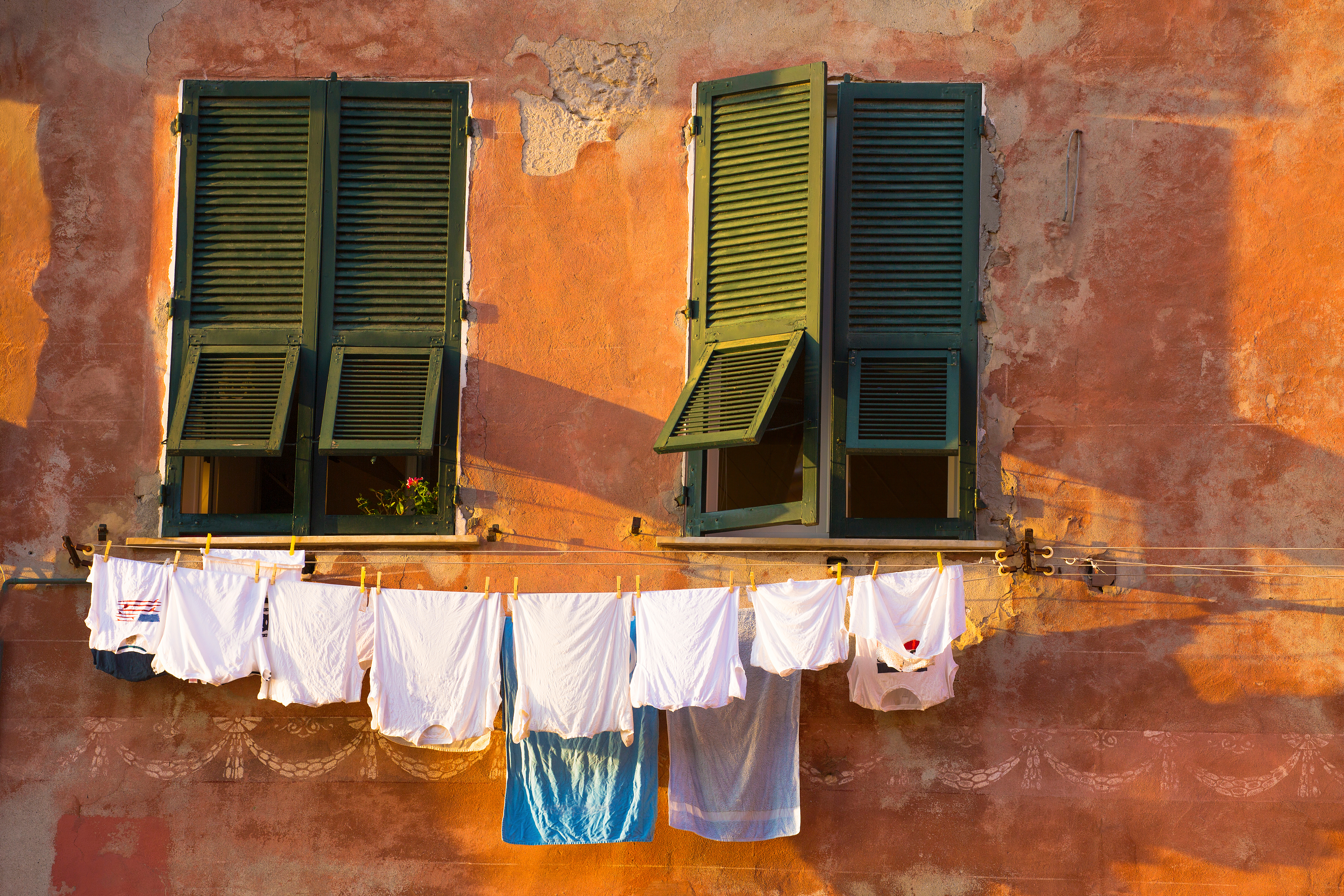 Traditionelt vasketøj hænger på en farverig orange facade med grønne skodder i Vernazza, Cinque Terre, Italien