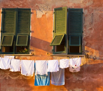 Traditionelt vasketøj hænger på en farverig orange facade med grønne skodder i Vernazza, Cinque Terre, Italien