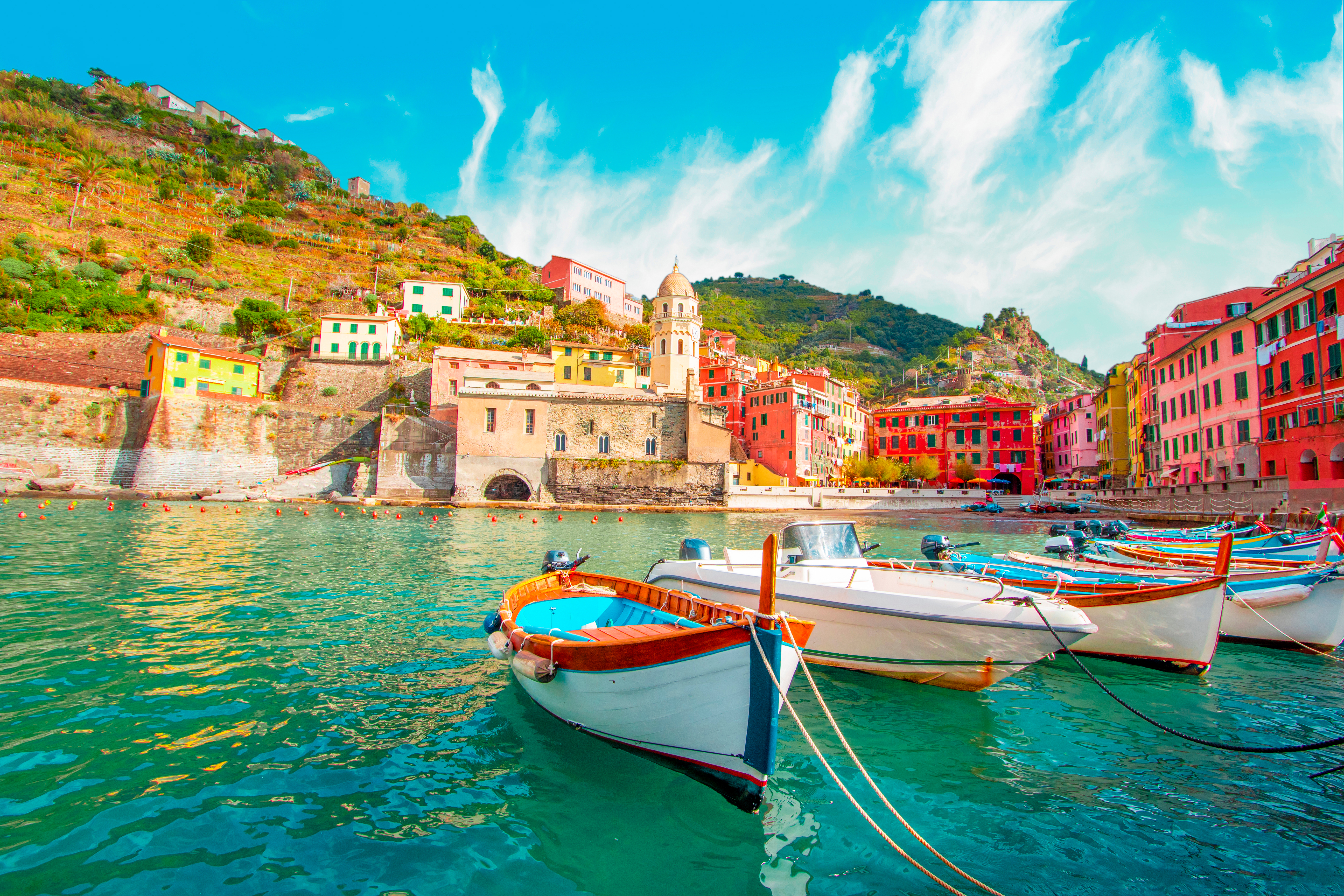 Malerisk udsigt over fiskerlandsbyen Vernazza i Cinque Terre, Italien, med farverige traditionelle huse bygget ind i klippesiden og en fiskerbåd i den lille havn ved det azurblå Middelhav