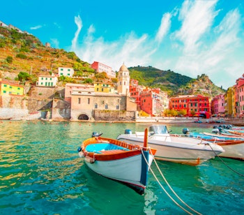 Malerisk udsigt over fiskerlandsbyen Vernazza i Cinque Terre, Italien, med farverige traditionelle huse bygget ind i klippesiden og en fiskerbåd i den lille havn ved det azurblå Middelhav