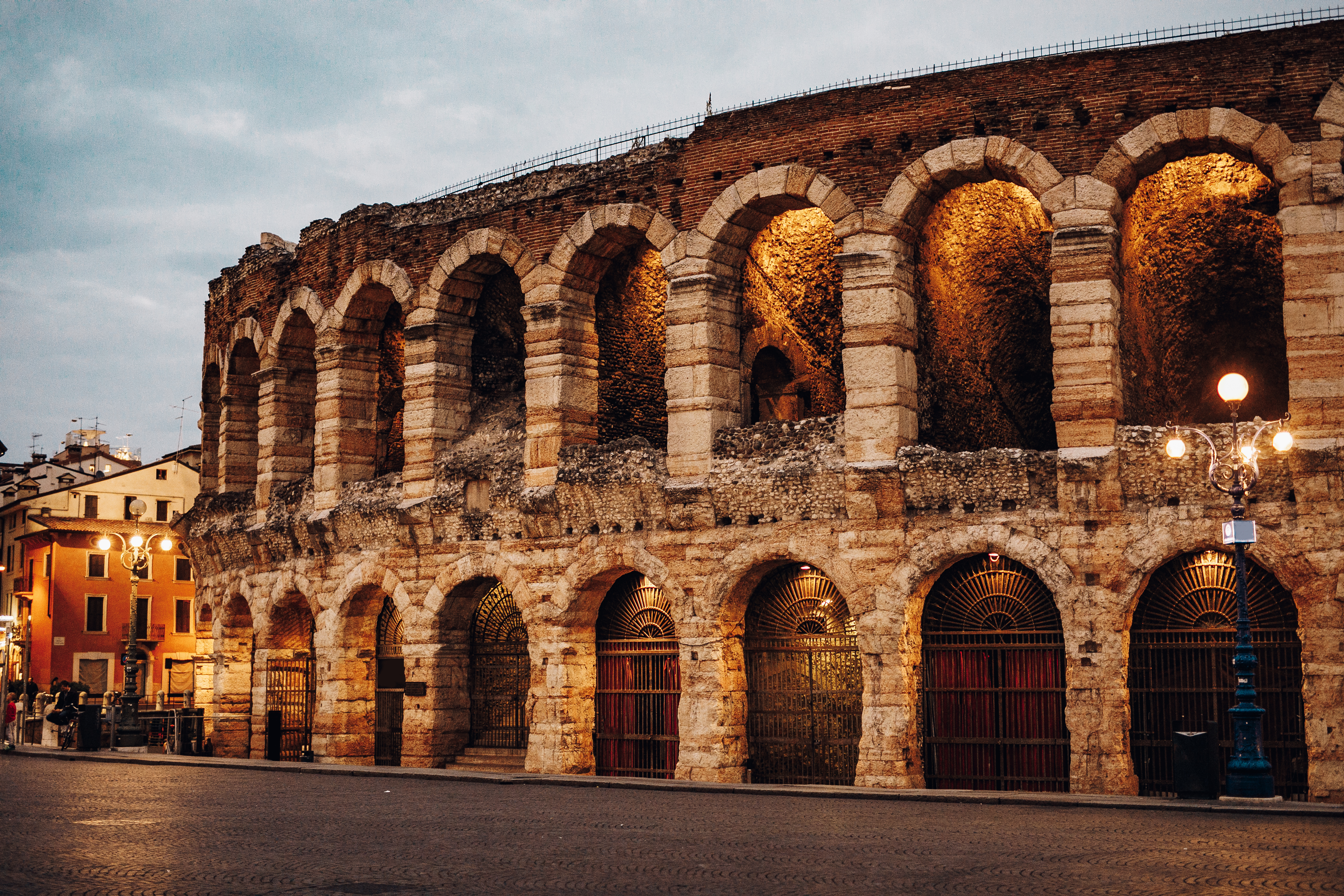 Den antikke romerske Arena di Verona oplyst i aftenlys med gyldne nuancer, der fremhæver de historiske buer og stenarkitektur i Verona, Italien