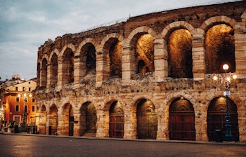 Den antikke romerske Arena di Verona oplyst i aftenlys med gyldne nuancer, der fremhæver de historiske buer og stenarkitektur i Verona, Italien