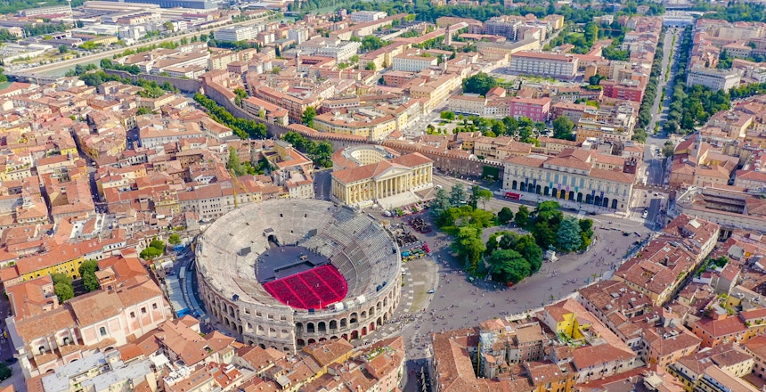 Betagende luftfoto over Veronas historiske bycentrum om sommeren, med fokus på det antikke romerske amfiteater Arena di Verona omgivet af terrakottafarvede tage og middelalderlig arkitektur